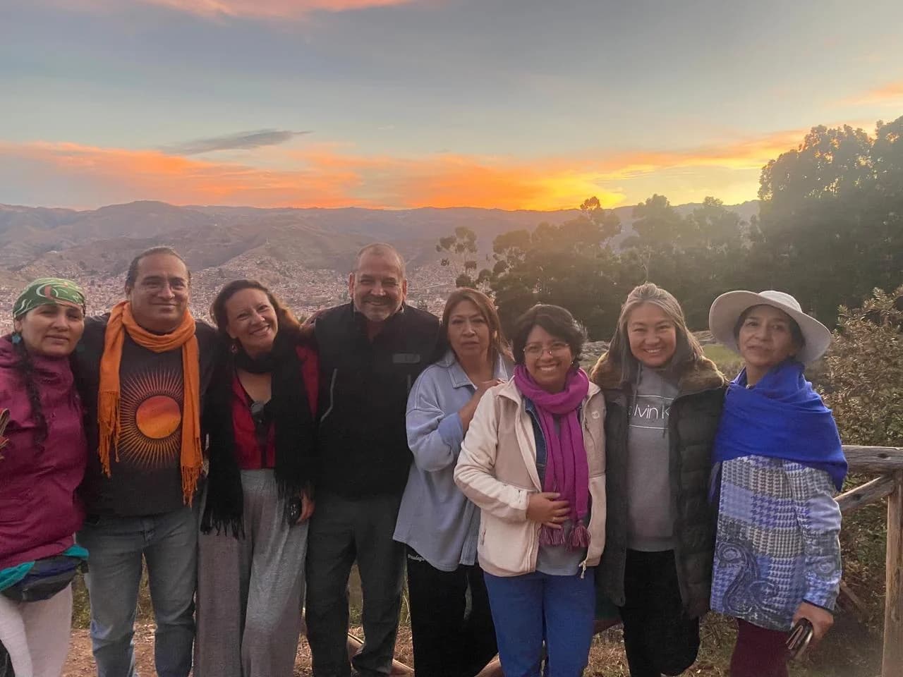 Un grupo reunido al aire libre frente a un paisaje de montañas al atardecer